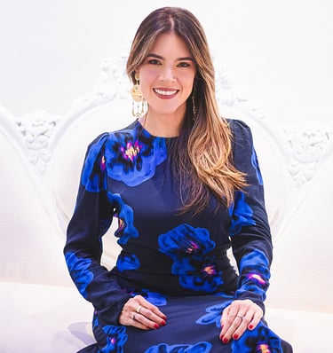 Natalia Devia sonriendo, sentada en un sillón blanco tallado, vestido azul floral