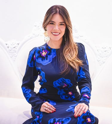 Natalia Devia sonriendo, sentada en un sillón blanco tallado, vestido azul floral