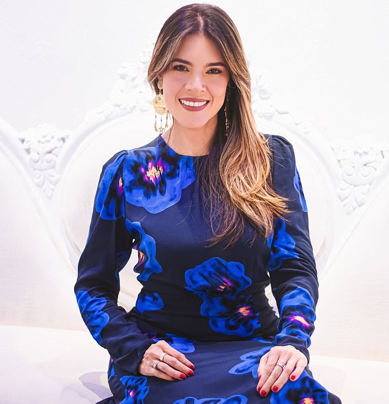 Natalia Devia sonriendo, sentada en un sillón blanco tallado, vestido azul floral